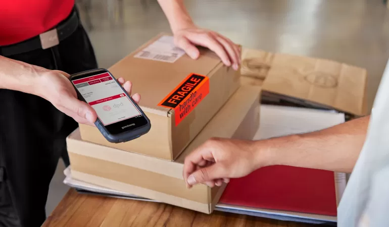 Klientka korzystająca z telefonu do skanowania kodu QR paczki w punkcie DPD Pickup, pracownik przygotowuje do wydan