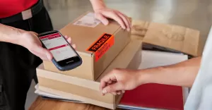 Klientka korzystająca z telefonu do skanowania kodu QR paczki w punkcie DPD Pickup, pracownik przygotowuje do wydan