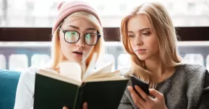 cheerful two women friends sitting cafe reading book